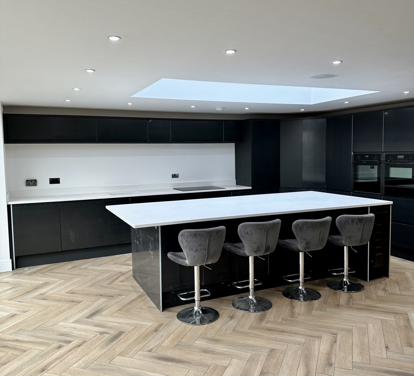 Modern black and white kitchen with sleek island and herringbone wood flooring.