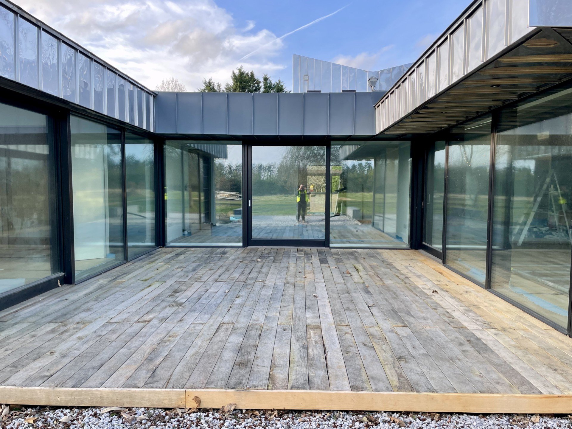 Modern home with glass walls and wooden deck blending with landscaped surroundings.